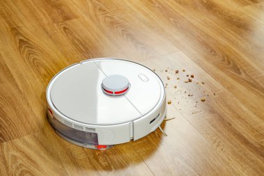 Robotik elektrik süpürgesi ahşap zemindeki toprağı kaldırıyor.