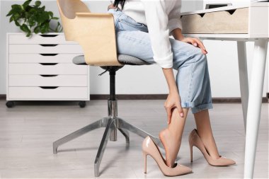 Woman rubbing sore leg in office, closeup