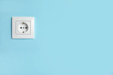Power socket on light blue wall, space for text. Electrical supply