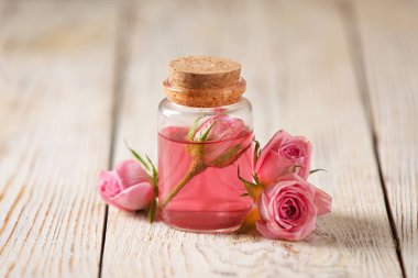 Bottle of essential rose oil and flowers on white wooden table clipart