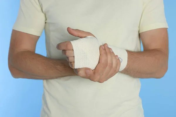 Man with hand wrapped in medical bandage on light blue background, closeup