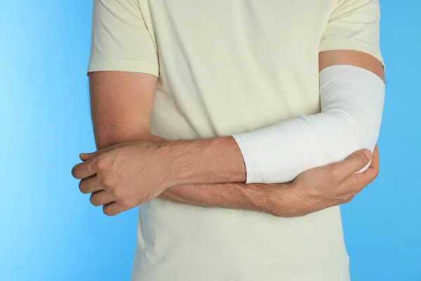 Mann Mit Arm Medizinischer Binde Auf Hellblauem Hintergrund Nahaufnahme — Stockfoto
