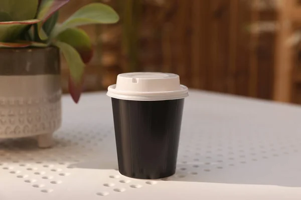 Takeaway paper cup with plastic lid on white table indoors