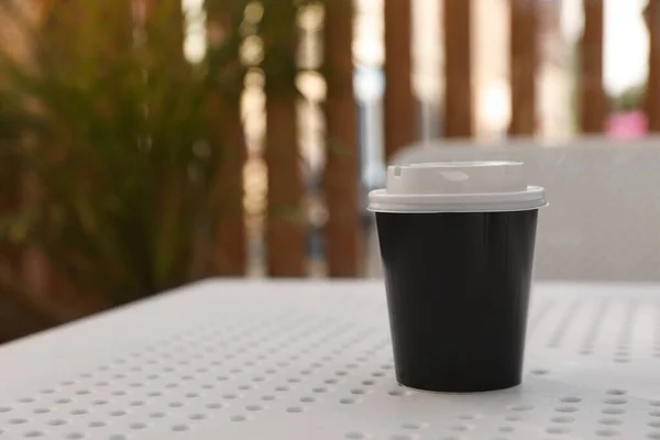 Takeaway paper cup with plastic lid on white table indoors, space for text