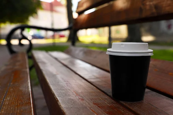 Takeaway paper cup with plastic lid on wooden bench outdoors, space for text