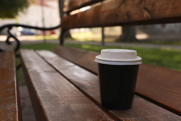 Takeaway paper cup with plastic lid on wooden bench outdoors, space for text