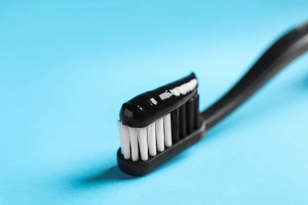Brush with charcoal toothpaste on light blue background, closeup