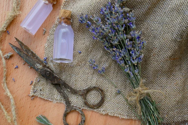 Beautiful lavender flowers, bottles of essential oil and scissors on wooden table, flat lay