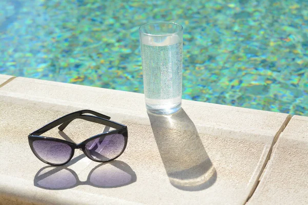 Stylové Sluneční Brýle Sklenice Vody Blízkosti Venkovního Bazénu Slunečného Dne — Stock fotografie