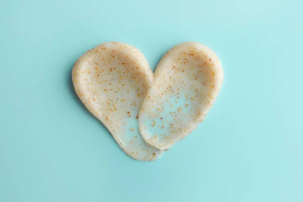 Samples of face scrub in shape of heart on light blue background, top view