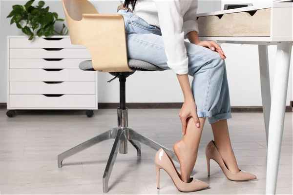 Woman rubbing sore leg in office, closeup
