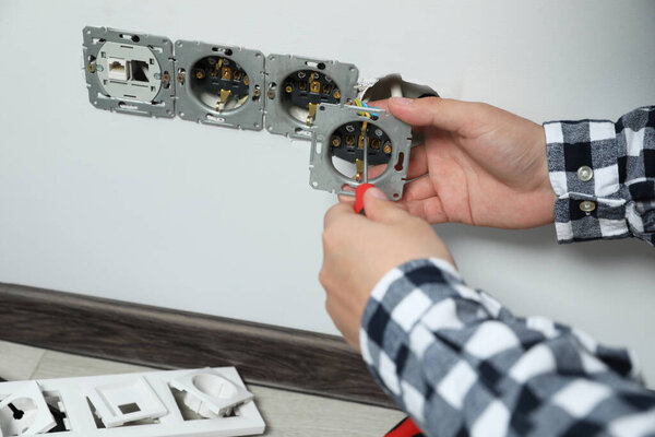 Электрик с отверткой для ремонта розетки в помещении, крупный план