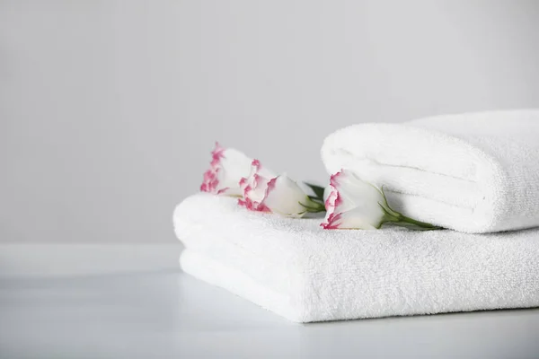 Folded soft towels with flowers on white table, space for text