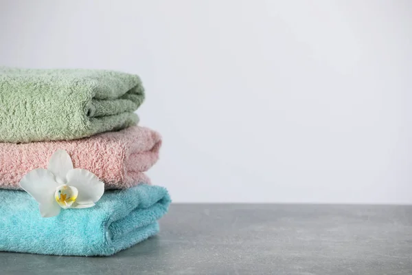 Stacked soft colorful towels with flower on grey table, space for text