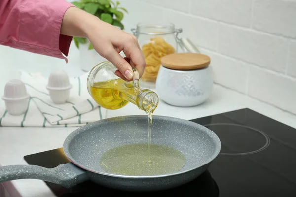 Woman pouring oil from jug into frying pan in kitchen, closeup