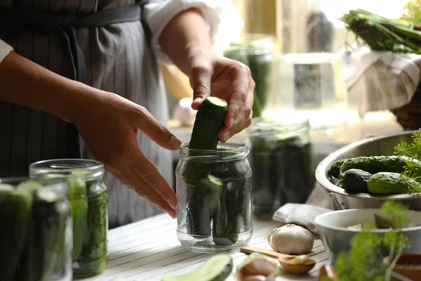 Woman putting cucumbers into jar in kitchen, closeup. Canning vegetables