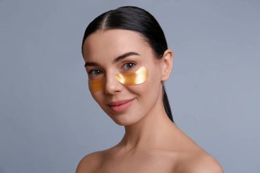 Gri arka planda göz bantları olan güzel genç bir kadın.