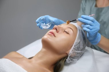 Kozmetik uzmanı salonda müşterinin yüzüne kimyasal kabuk ürünü uyguluyor.
