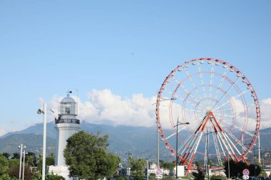 Batumi, Georgia - 12 Ekim 2022: Dağların yakınlarındaki şehirde dönme dolap ve deniz feneri