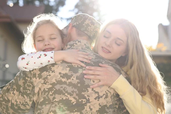 Daughter and wife hugging soldier in Ukrainian military uniform outdoors. Family reunion
