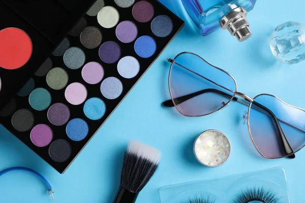 Set of makeup products and sunglasses on light blue background, flat lay