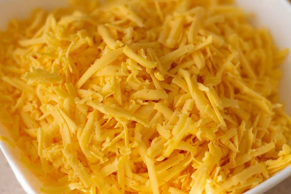 Sliced cheese in a kitchen plate. Cutting on a grater. Natural dairy ingredient for cooking. Delicious, healthy, vegetarian and diet food. Closeup photo