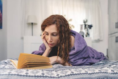 A woman is relaxing at home. Lying in bed and reading a book