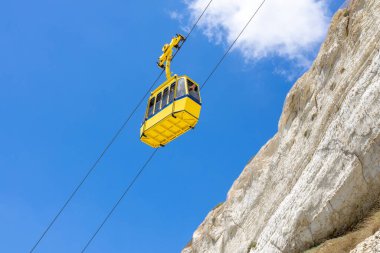 Yellow funicular climbing up the mountain. White rock and blue sky in the background. Rosh Hanikra, North Israel