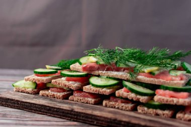 İnce buğday ekmeğinde kırmızı somon balıklı sandviçler beslenme için taze salatalık, limon ve dereotları kompozisyonda görülebilir, ahşap bir tahtanın üzerinde büyük bir yığın