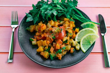 Siyah bir tabakta Ratatouille, farklı sebzeleri bir güveçte boyadı, taze maydanoz yaprakları ve limon dilimleri ile, pembe ahşap arka planda, birçok ülke için uygun fiyatlı bir yemek.