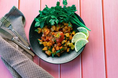Siyah bir tabakta Ratatouille, farklı sebzeleri bir güveçte boyadı, taze maydanoz yaprakları ve limon dilimleri ile, pembe ahşap arka planda, birçok ülke için uygun fiyatlı bir yemek.