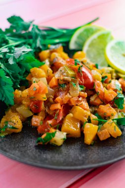 Siyah bir tabakta Ratatouille, farklı sebzeleri bir güveçte boyadı, taze maydanoz yaprakları ve limon dilimleri ile, pembe ahşap arka planda, birçok ülke için uygun fiyatlı bir yemek.