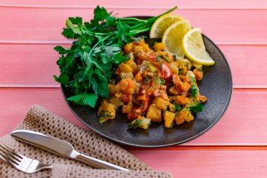 Siyah bir tabakta Ratatouille, farklı sebzeleri bir güveçte boyadı, taze maydanoz yaprakları ve limon dilimleri ile, pembe ahşap arka planda, birçok ülke için uygun fiyatlı bir yemek.