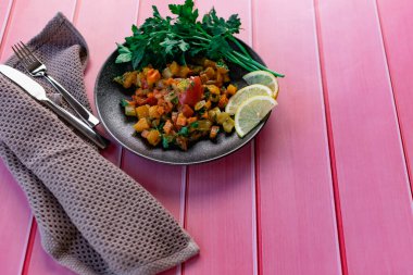 Siyah bir tabakta Ratatouille, farklı sebzeleri bir güveçte boyadı, taze maydanoz yaprakları ve limon dilimleri ile, pembe ahşap arka planda, birçok ülke için uygun fiyatlı bir yemek.