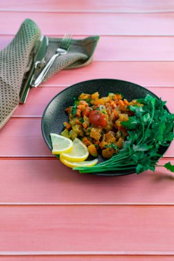 Siyah bir tabakta Ratatouille, farklı sebzeleri bir güveçte boyadı, taze maydanoz yaprakları ve limon dilimleri ile, pembe ahşap arka planda, birçok ülke için uygun fiyatlı bir yemek.