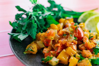 Siyah bir tabakta Ratatouille, farklı sebzeleri bir güveçte boyadı, taze maydanoz yaprakları ve limon dilimleri ile, pembe ahşap arka planda, birçok ülke için uygun fiyatlı bir yemek.