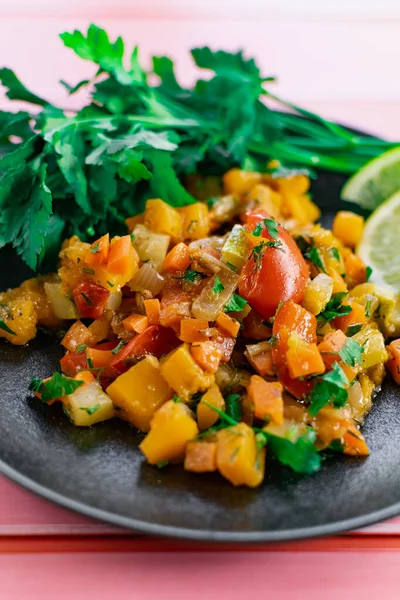 Siyah bir tabakta Ratatouille, farklı sebzeleri bir güveçte boyadı, taze maydanoz yaprakları ve limon dilimleri ile, pembe ahşap arka planda, birçok ülke için uygun fiyatlı bir yemek.