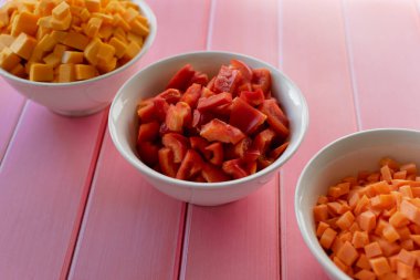 Taze Bulgar biberi, pembe ahşap arka planda, bir kasede doğranmış taze kırmızı biber, mutfakta pişirmek için taze sebzeler, hazır malzemeler.