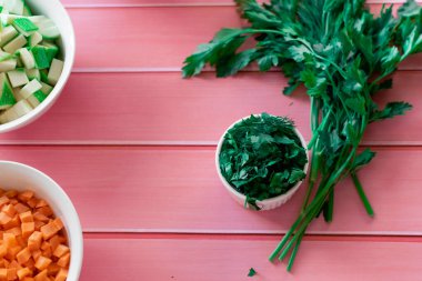 Taze yeşil maydanoz ve pembe ahşap arka planda dereotu, mutfakta yemek pişirmek için hazırlanan malzemeler, baharat yerine kokulu gıda katkı maddeleri.