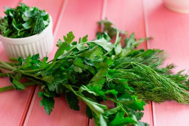 Taze yeşil maydanoz ve pembe ahşap arka planda dereotu, mutfakta yemek pişirmek için hazırlanan malzemeler, baharat yerine kokulu gıda katkı maddeleri.