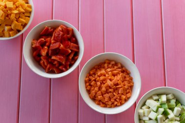 Farklı doğranmış taze sebzeler, farklı renkte meyveler, pembe ahşap bir masa, mutfakta yemek pişirme hazırlığı, renkli malzemeler.