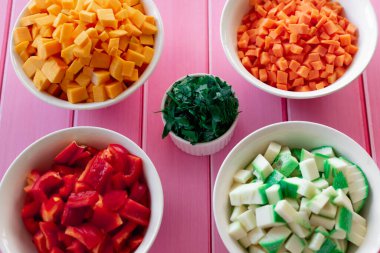 Farklı doğranmış taze sebzeler, farklı renkte meyveler, pembe ahşap bir masa, mutfakta yemek pişirme hazırlığı, renkli malzemeler.