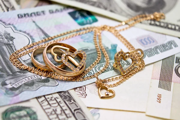 Wedding rings, gold chain and earrings in the form of hearts lie on money — Stock Photo, Image