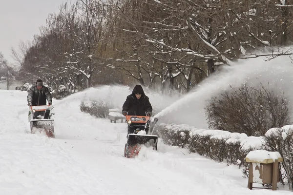 Werknemers van gemeentelijke diensten verwijderen de sneeuw uit de stoep met de hulp van motorvoertuigen — Stockfoto