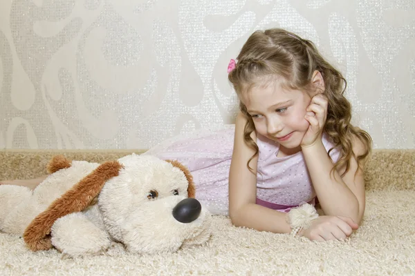 Menina deitada no tapete com um cachorro de pelúcia — Fotografia de Stock