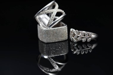 Siyah ayna yüzeyinde farklı şekil ve boyutlarda gümüş kadın yüzükleri.