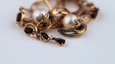 Altın küpeler ve değerli taşlar ve incilerle beyaz bir yüzey üzerinde döner.