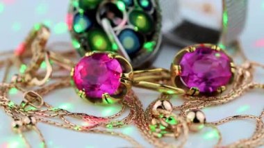 Büyük kırmızı yakut, yüzük, zincir ve kolye ile altın küpeler beyaz bir yüzey üzerinde döner