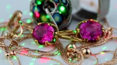 Büyük kırmızı yakut, yüzük, zincir ve kolye ile altın küpeler beyaz bir yüzey üzerinde döner