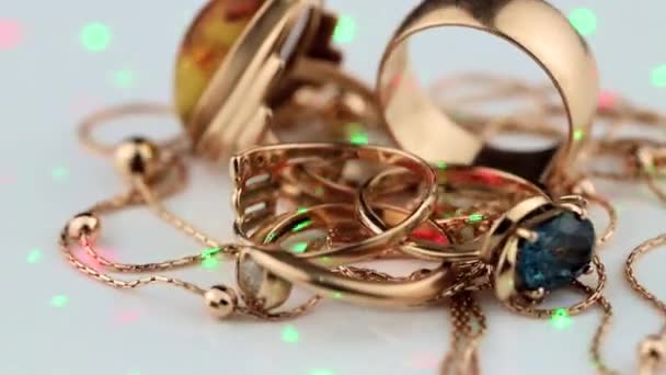 Os anéis de ouro com âmbar, diamante e safira giram em um topo branco e são iluminados por feixes de laser coloridos — Vídeo de Stock